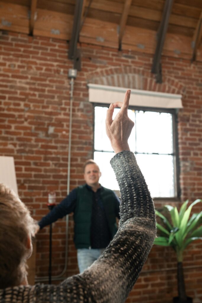 A person raising their hand during an indoor presentation with a brick wall background.